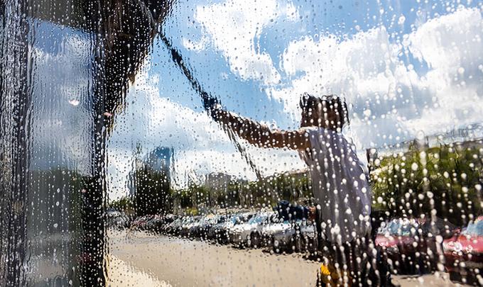 A person cleaning a large window with a squeegee on a sunny day.